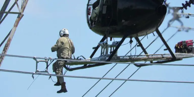 Trabajador reparando lineas de alto voltaje desde un helicóptero.