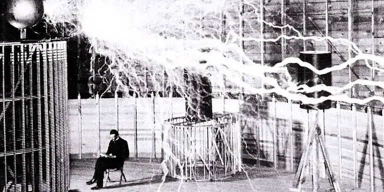 Nikola Tesla leyendo en su taller junto a una bobina eléctrica.